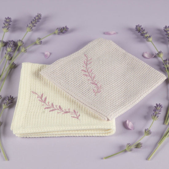 Folded fabric with embroidered design surrounded by lavender flowers on a light purple background